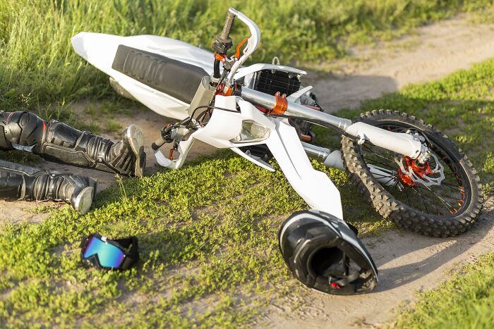 A white dirt bike crashed on a grassy track next to a helmet and boots, illustrating potential pain reactions.