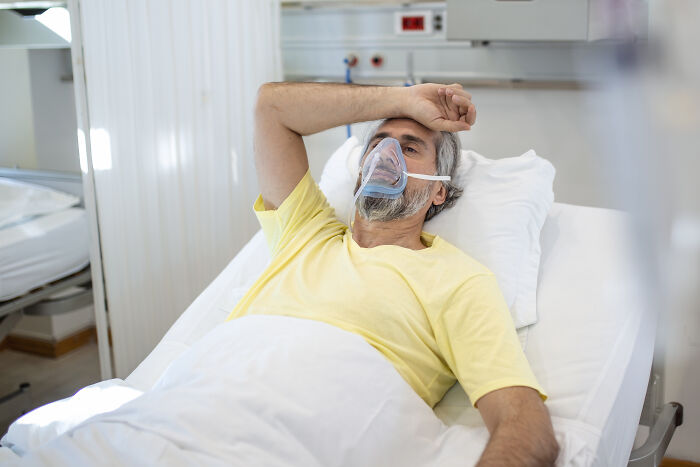 A man with an oxygen mask in a hospital bed, experiencing extreme illness and sickness.