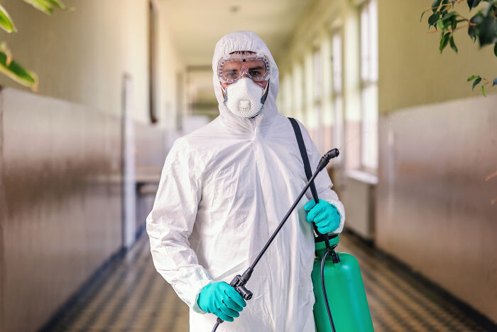 Person in protective suit and mask holding disinfectant sprayer
