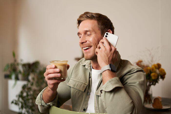 A cheerful man talking on a smartphone with a warm drink, capturing satisfying stories of people