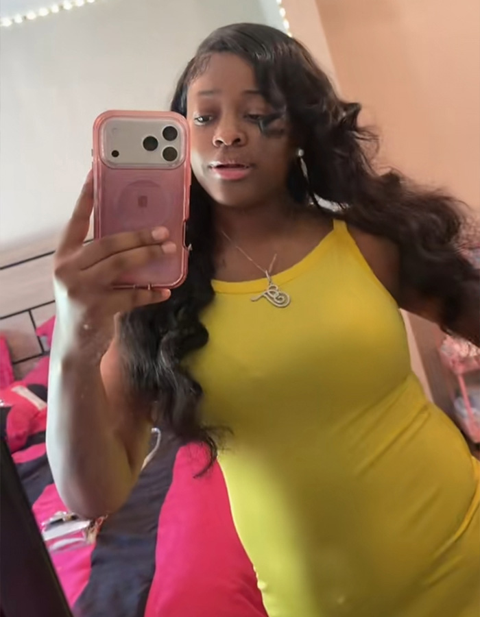 A pregnant woman in a yellow dress takes a mirror selfie with her phone. A pregnant woman in a yellow dress takes a mirror selfie with her phone.