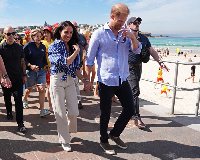 Prince Harry and Meghan Markle walking hand in hand at a sunny beachside location