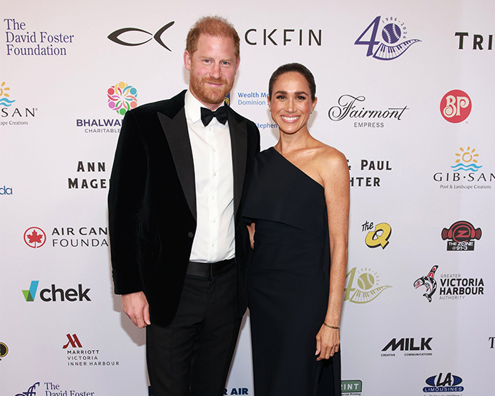 Prince Harry and Meghan Markle posing at a formal event with charity logos in background