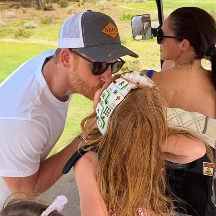 Prince Harry kissing a child while Meghan Markle looks on during outdoor golf outing