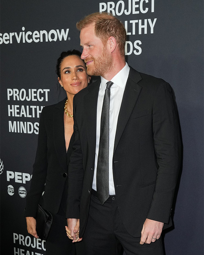 Prince Harry and Meghan Markle holding hands at an event. They are issuing a contentious response to King Charles' letter.