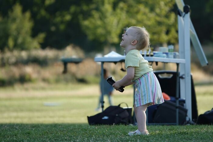A young toddler smiling in a grassy park, a candid moment from a wedding event