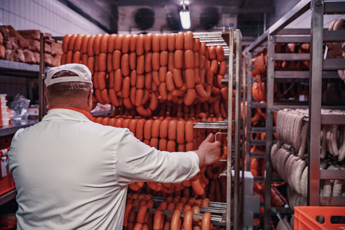 A butcher in a processing plant with rows of sausages, representing industry secrets in food production.