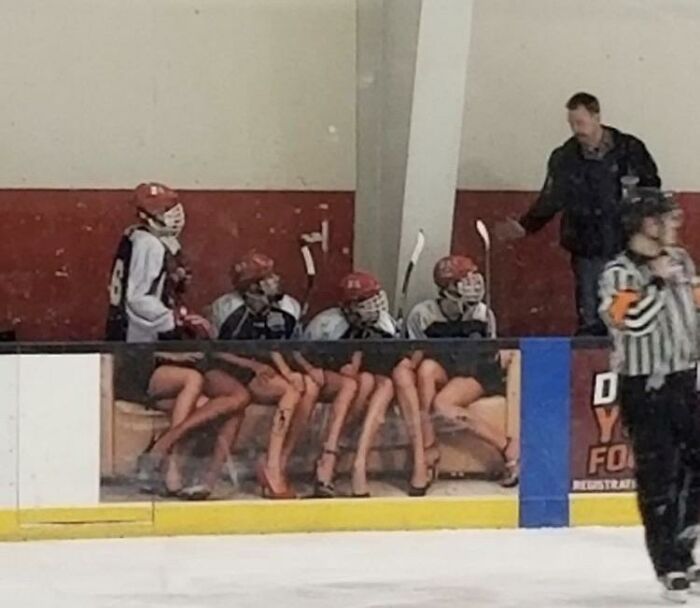 Confusing perspective of hockey players on a bench who appear to have long legs in heels due to a banner advertisement.