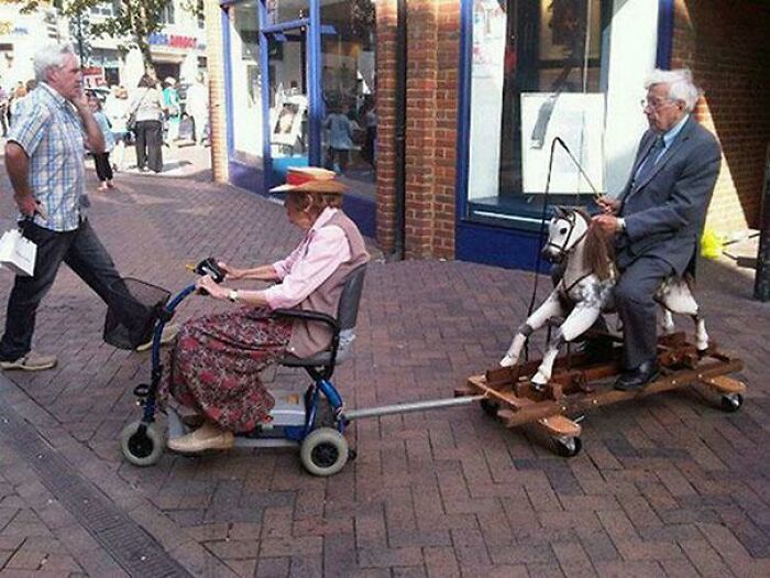 An older woman on a mobility scooter pulls an older man riding a hobby horse, creating unhinged images.