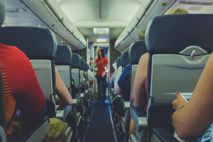 Airplane interior with passengers seated and a cabin crew member standing in the aisle, ready to deal with various issues.