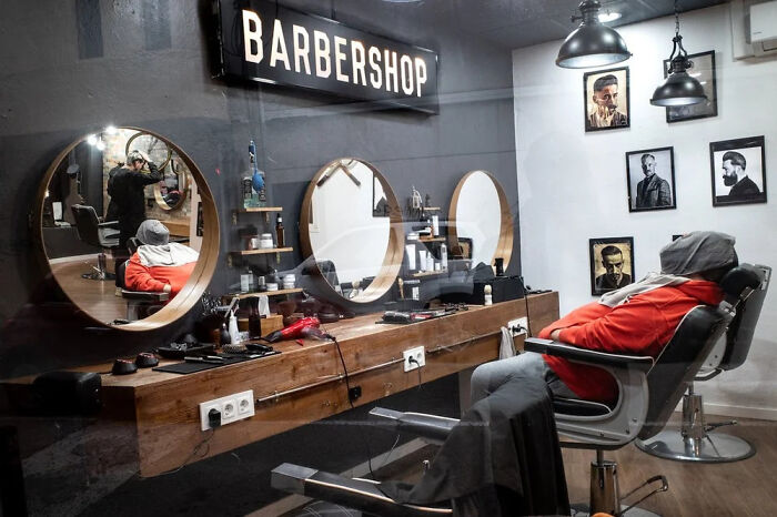 A man waiting in a modern barbershop with sleek mirrors and industrial lights, a unique scene captured by a street photographer.