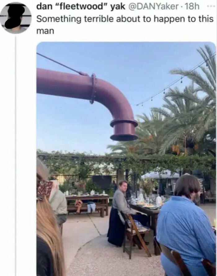 A man looks at the camera while a giant curved pipe is above his head, ready to drop on him, a hilarious photo.
