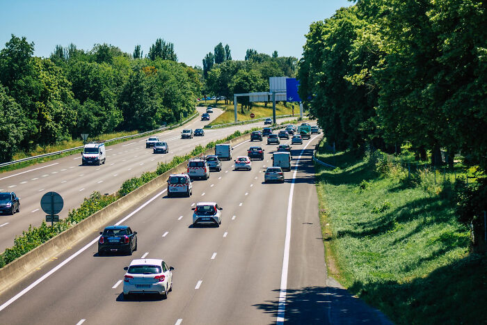A busy road with multiple vehicles and green trees, highlighting the need for road users to learn about speed cameras.