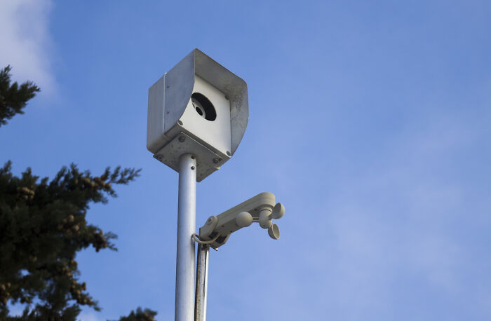 A speed camera on a pole against a blue sky, an important detail for road users learning about speed camera signs.