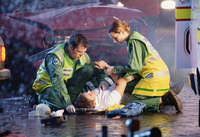 Paramedics tending to an injured person on a stretcher after a car accident, telling stories that swear are 100% true.