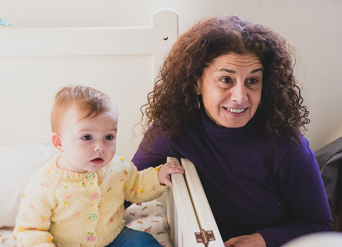 A MIL babysits a baby girl in her nursery while looking thoughtful and smiling A MIL babysits a baby girl in her nursery while looking thoughtful and smiling