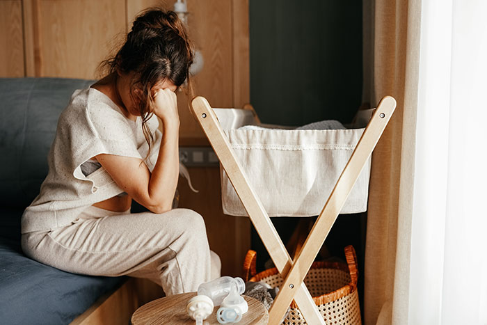 A worried woman sitting on the edge of a bed next to a nursery crib. A worried woman sitting on the edge of a bed next to a nursery crib.