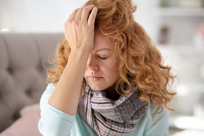 A woman with red curly hair, wearing a scarf, holds her head in her hand, experiencing inheritance drama. A woman with red curly hair, wearing a scarf, holds her head in her hand, experiencing inheritance drama.