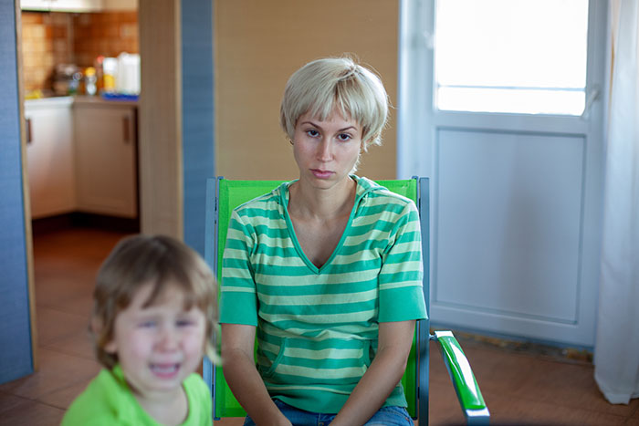 A woman with short blonde hair in a striped shirt sits, looking upset, with a crying child in the foreground, showing inheritance drama. A woman with short blonde hair in a striped shirt sits, looking upset, with a crying child in the foreground, showing inheritance drama.