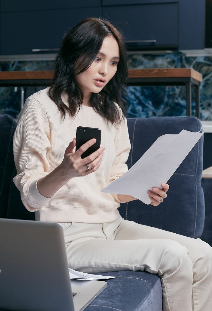 A shocked woman holding a phone and document, reading unbelievable relationship revenge stories.