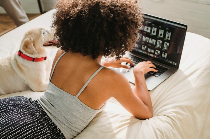 A woman on a bed typing on a laptop with her dog, writing relationship revenge stories