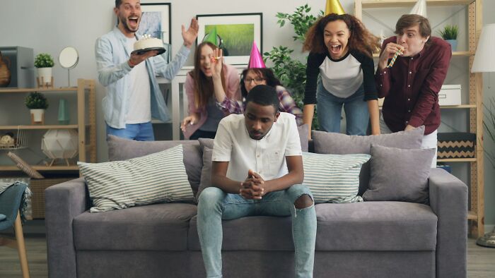 A sad man on a couch surrounded by celebrating friends, illustrating relationship revenge stories