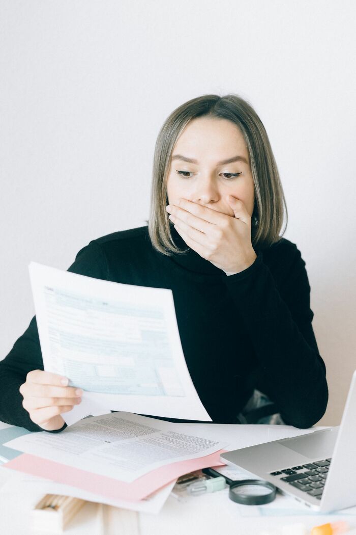 Shocked woman covers her mouth while reading a paper, depicting a dramatic relationship revenge consequence.
