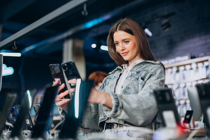 A young woman comparing smartphones in a tech store, showcasing creative ideas for relationship revenge.