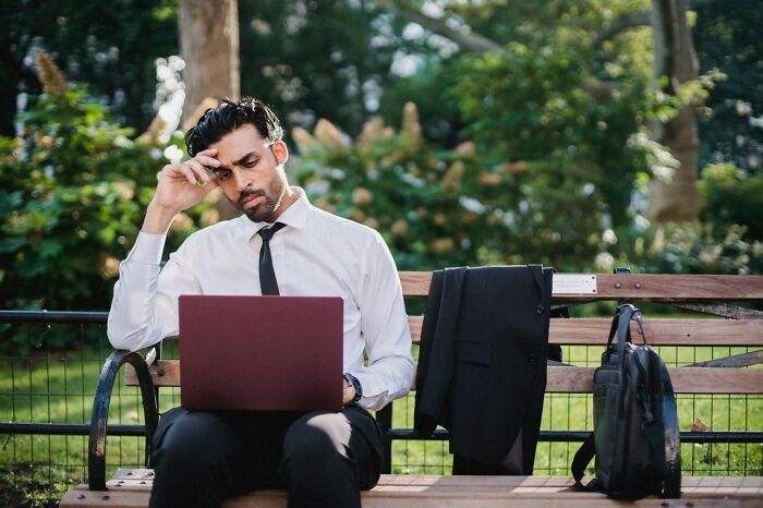 A stressed businessman looking at his laptop on a park bench, sparking dramatic relationship stories.