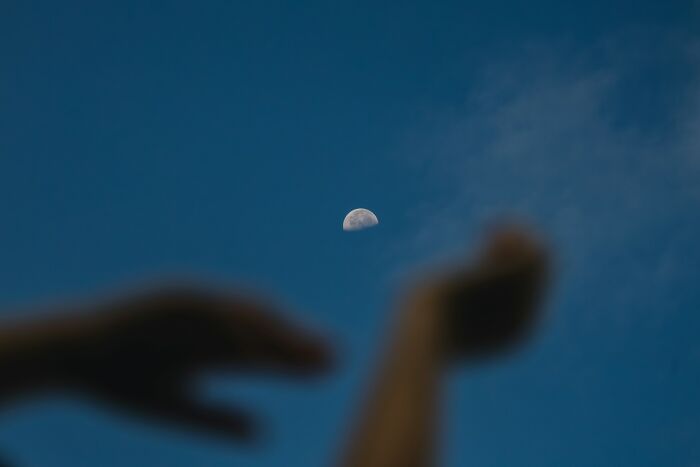 Blurry hands reaching towards the half moon in a clear blue sky, illustrating stupid things people said.