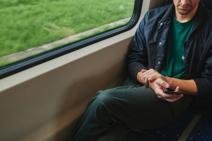 A man sitting on a train, engrossed in his phone, showing a scene people overheard.