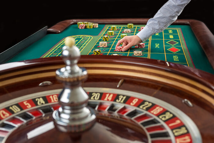 A hand placing chips on a roulette table, with a roulette wheel in the foreground, showing surprising things wealthy people buy.