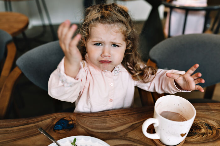 A cute little girl gesturing with frustration next to a cup, representing satisfying stories
