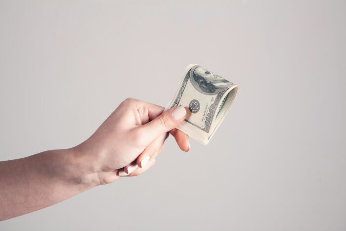 A hand holding a stack of hundred-dollar bills, illustrating the cost clients pay to lawyers for their stupid actions.