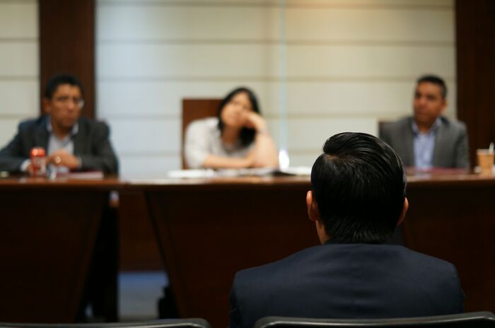A client sitting with their back to the camera facing three lawyers, one of whom looks bored, representing clients with stupid decisions.