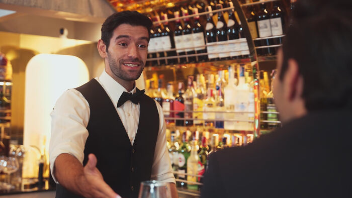 A friendly bartender welcoming a guest, displaying open body language to read people.