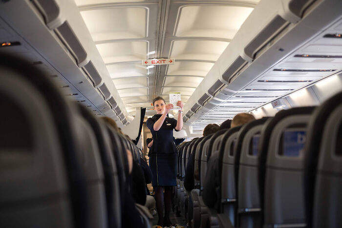 A flight attendant standing in the aisle of an airplane, demonstrating professional behaviors and posture.