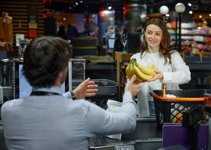 A woman handing bananas to a cashier, demonstrating everyday behaviors and social interaction.