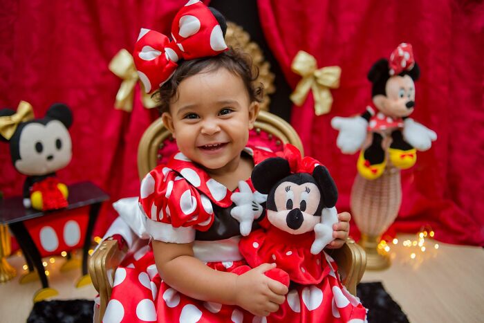 A smiling baby girl dressed as Minnie Mouse, showing joyful behaviors and expressions.