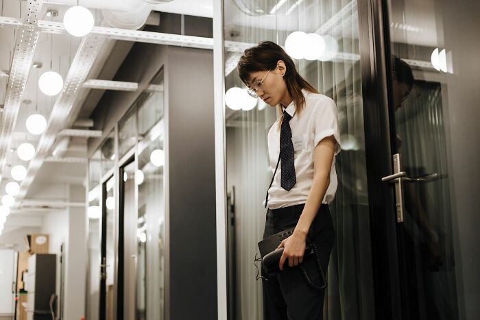 A thoughtful person in an office hallway looking down, showcasing reflective body language behaviors