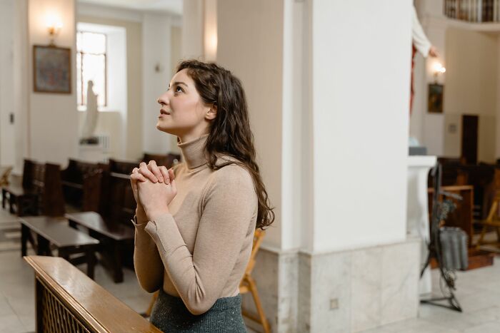 A young woman praying inside a church with folded hands, depicting behaviors of faith and hope