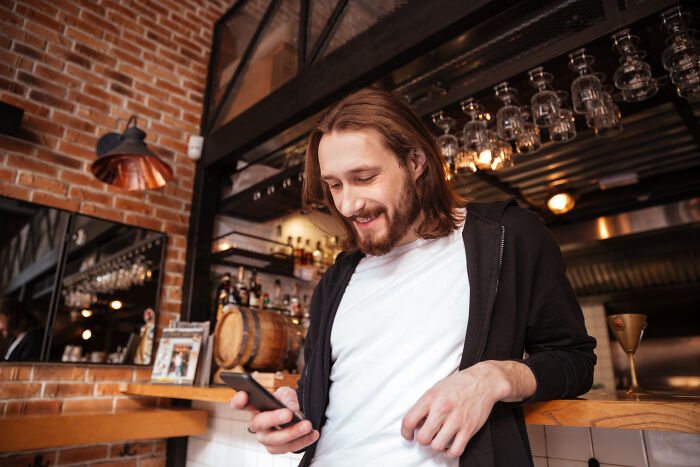 A happy young man looking at his smartphone, displaying relaxed behaviors that reveal personality.