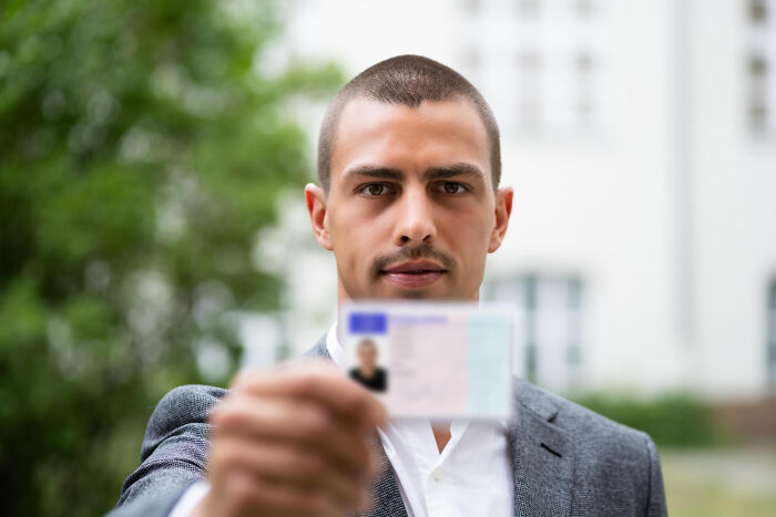 A man holding up an identification card close to the camera, showcasing behaviors that tell everything.