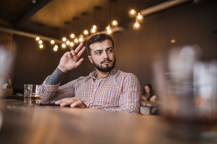 A man sitting at a bar gesturing with his hand, showing social behaviors and expressions