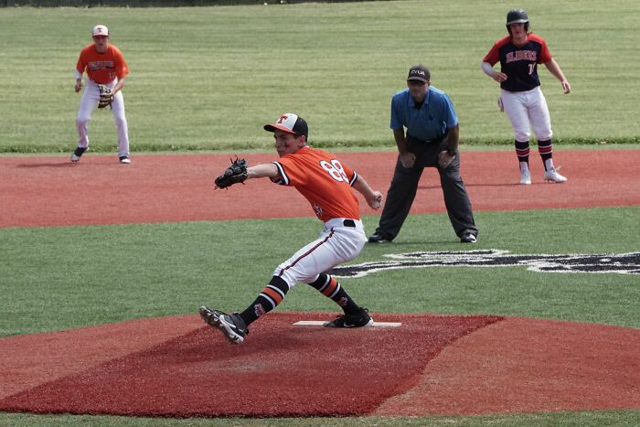 Baseball pitcher throwing ball during game with umpire and players in background