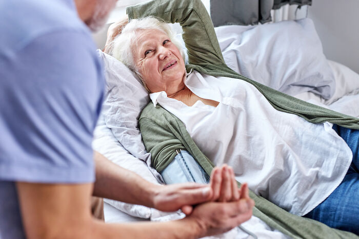 An older woman with white hair lays in bed, a man holding her hand, depicting pain reactions in elderly patients.