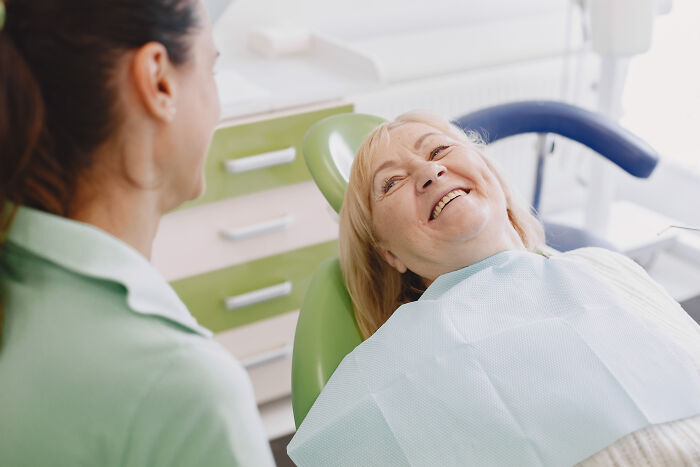 A smiling senior woman in a dental chair, showing her pain reactions and relief after a procedure.