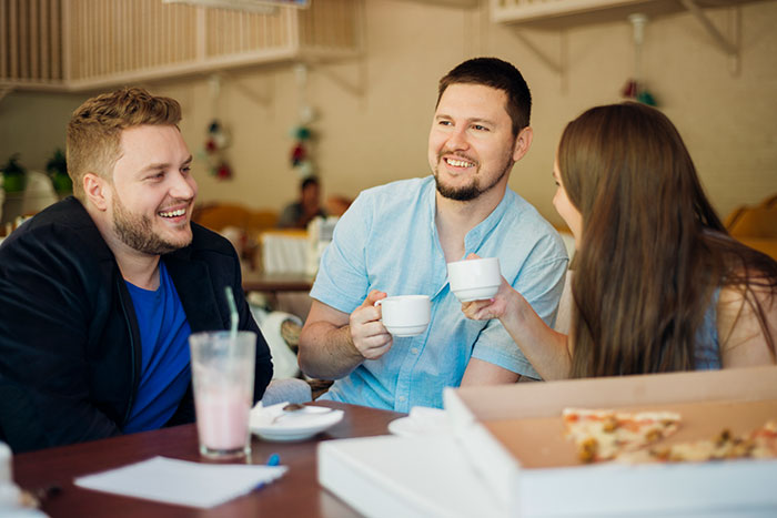 A group of friends, including a model, at a table with coffee and pizza, discussing a buddy needing a hot girlfriend and weight-loss coach. A group of friends, including a model, at a table with coffee and pizza, discussing a buddy needing a hot girlfriend and weight-loss coach.