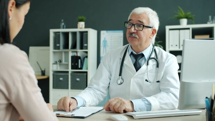 Older male doctor consulting female patient revealing sexist treatment