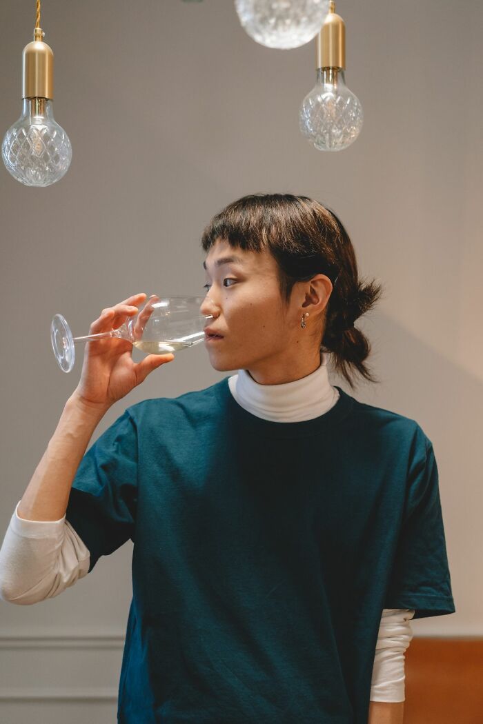 Person drinking wine under decorative light bulbs indoors